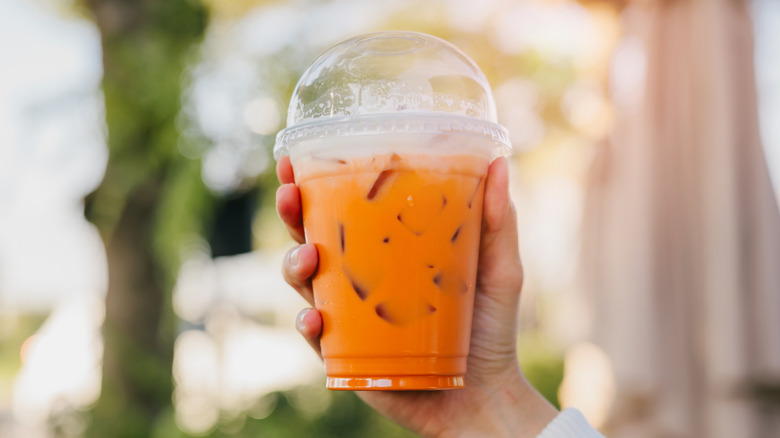 Hand holding plastic to-go cup of Thai iced tea