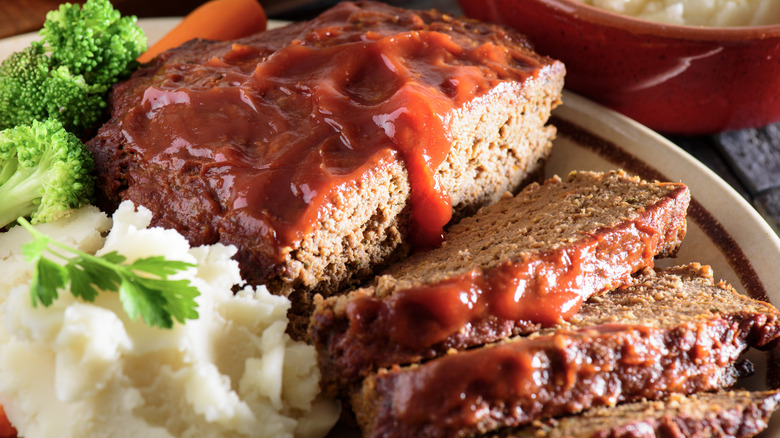 Tomato sauce-topped meatloaf with three slices cut on a plate with mashed potatoes and broccoli