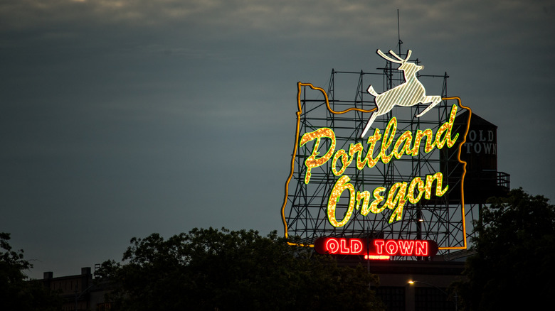 Lit-up large neon sign with the words Portland Oregon and a jumping deer against a night sky
