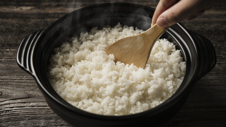 Stirring cooked rice in a black pot with a wooden spatula