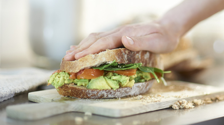 Hand pressing avocado sandwich
