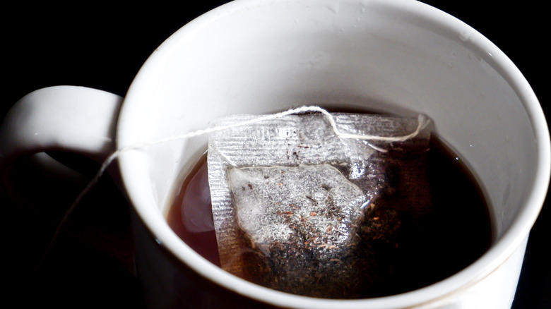 A tea bag steeping in a white mug of black tea
