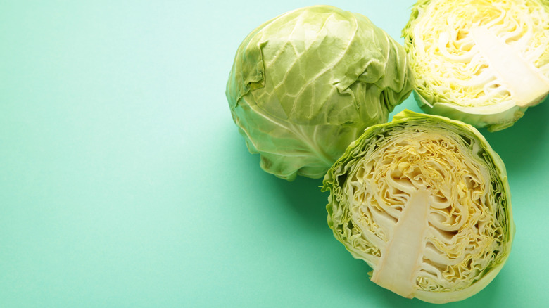 A green cabbage cut in half and sitting on a green background