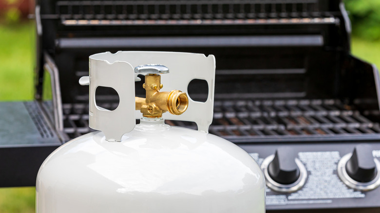 A white propane tank in front of an open grill