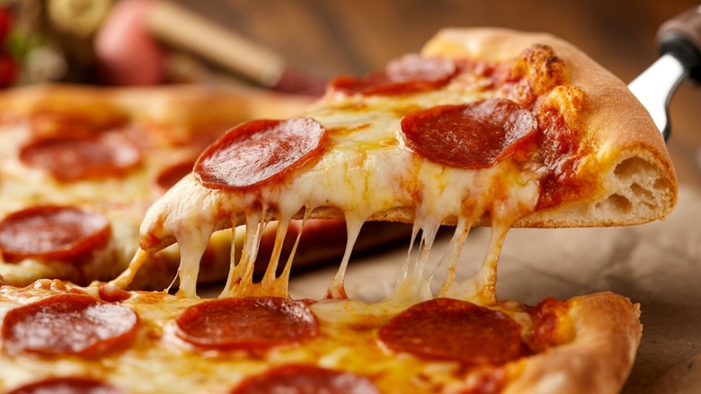 Person lifting slice of pepperoni pizza from the whole pie up close