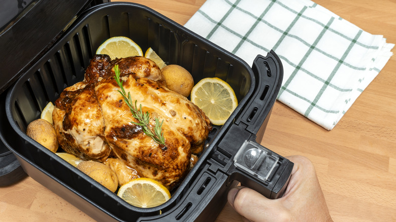 whole baked chicken in air fryer basket next to cloth