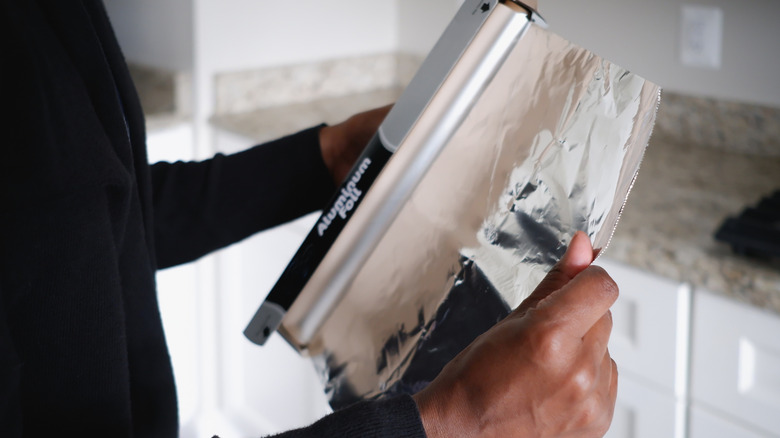 Person removing aluminum foil from the container
