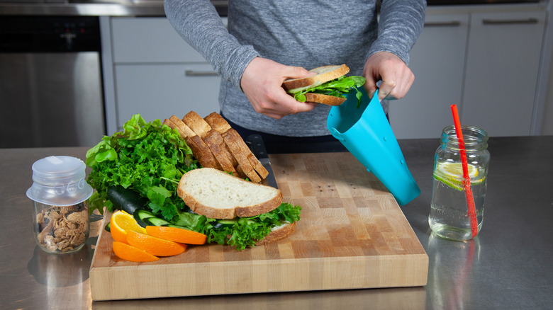 A person prepares lunch and places a sandwich into a blue food-grade silicone bag