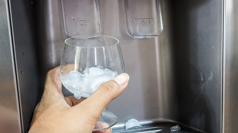 Person filling glass with ice from fridge dispenser