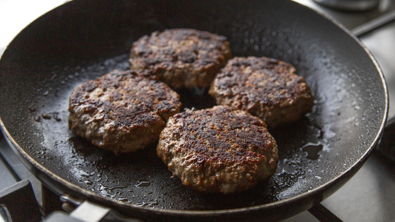 Four hamburger patties cooking in a frying pan