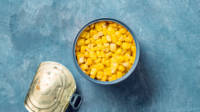 An opened can of corn with top peeled off on blue background