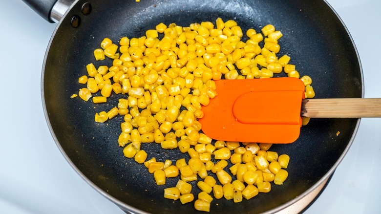 Corn kernels in sauté pan on stove being stirred with spatula