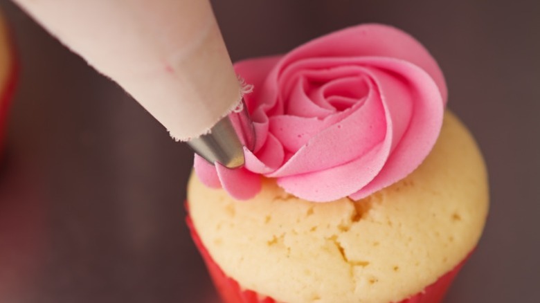 Using a piping bag to put pink flower on cupcake.