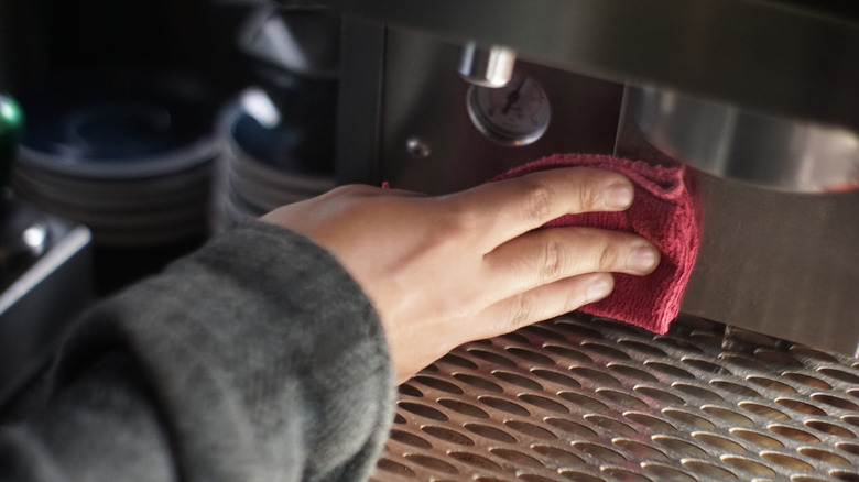 Hand wiping down a coffee maker with a towel