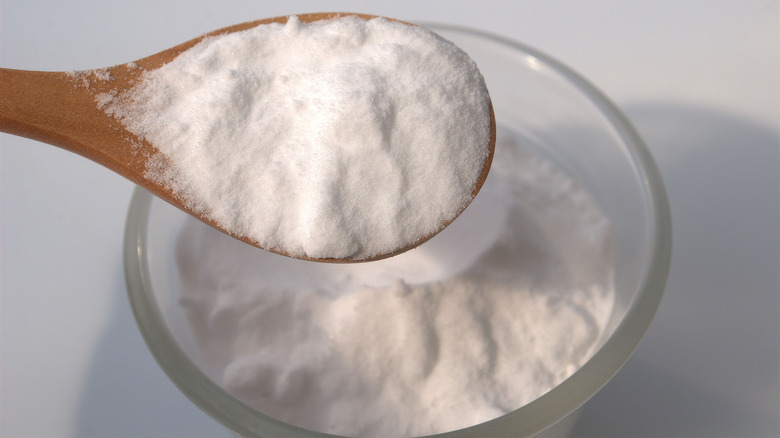 A glass bowl and a small wooden spoon of baking soda