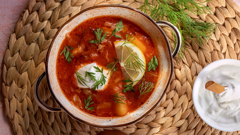 A bowl of tomato soup with a slice of lemon, fresh dill, and sour cream