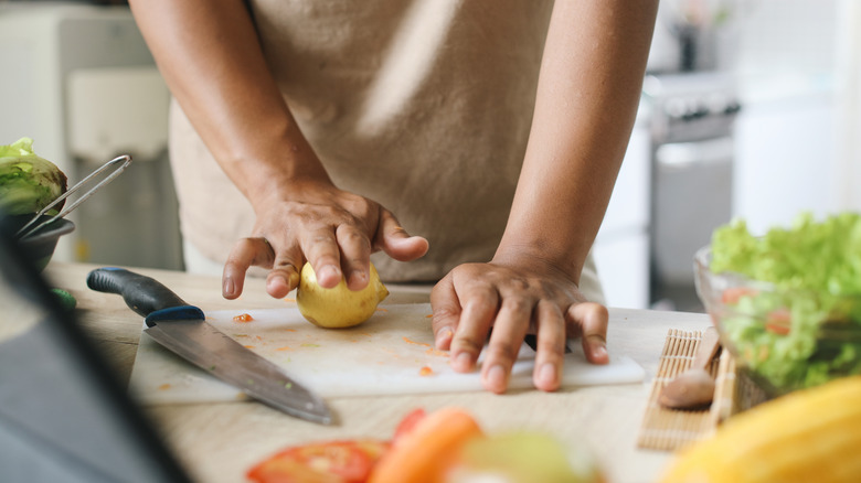 Person rolling a lemon on a dirty cutting board next to a knife