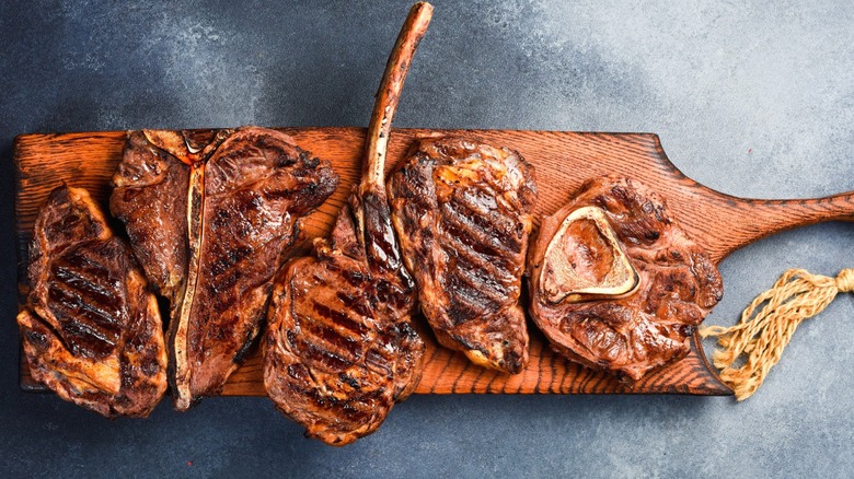 Several bone-in steaks on a cutting board.
