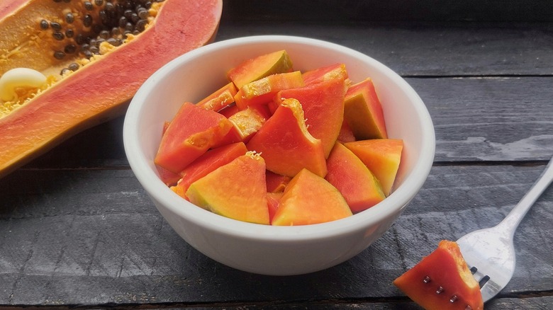 A bowl of cut papaya with a fork and half of a fresh papaya