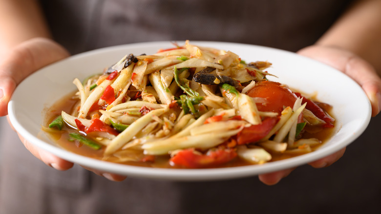 A server holds a plate of som tum, a Thai salad of green papaya