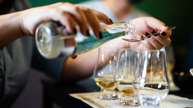 a person carefully adding a small spoonful of water to a whiskey glass