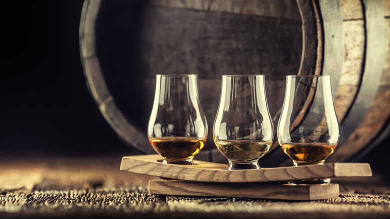 three whiskey glasses sit on a tray in front of a whiskey barrel