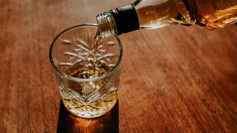 whiskey pouring from bottle into glass with ice cube