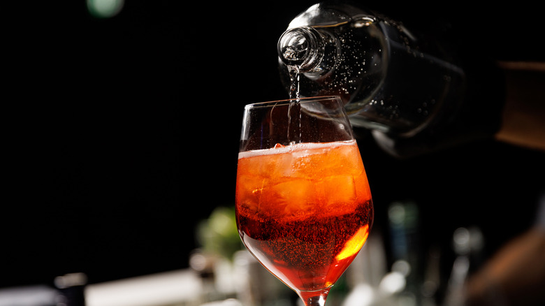 A close-up of someone making a fizzy Aperol spritz