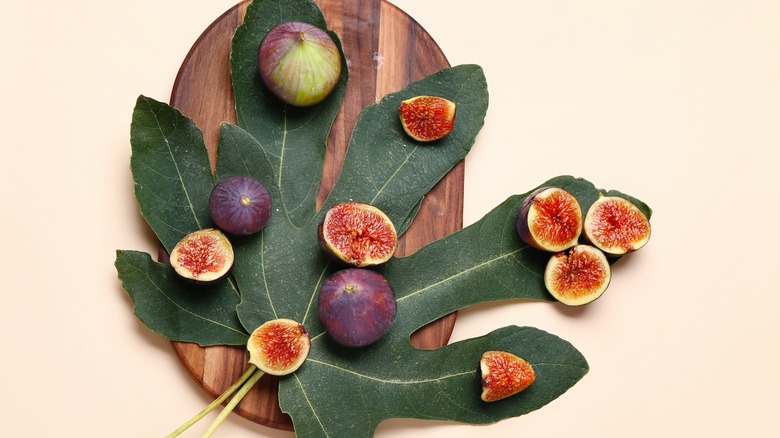 Whole figs and cut figs arranged on two large fig leaves on an oval wood cutting board