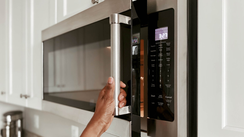Hand reaching up to open microwave