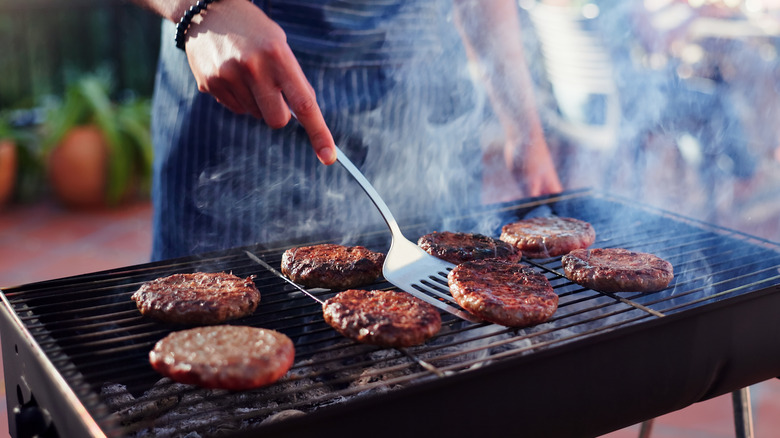 Spatula flipping burgers on outdoor charcoal grill