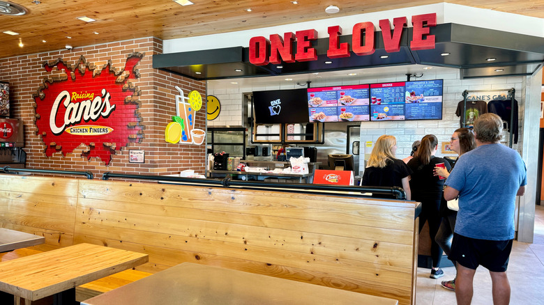 An interior view of a Raising Cane's restaurant with people waiting in line to the counter
