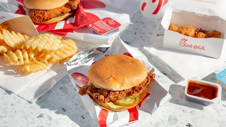 Chick-fil-A sandwich with chicken nuggets, sauce, and waffle fries nearby
