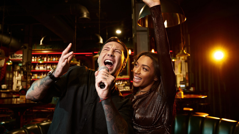 two happy people sing karaoke inside bar