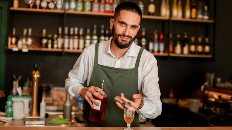 smiling bartender pours liquor into small ornate glass behind bar