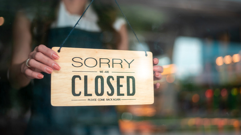 woman turns over sorry closed sign on door