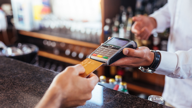 hand puts credit card into machine at bar
