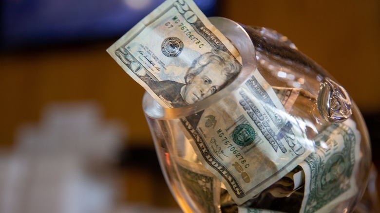 glass tip jar with twenty dollar bill sticking out