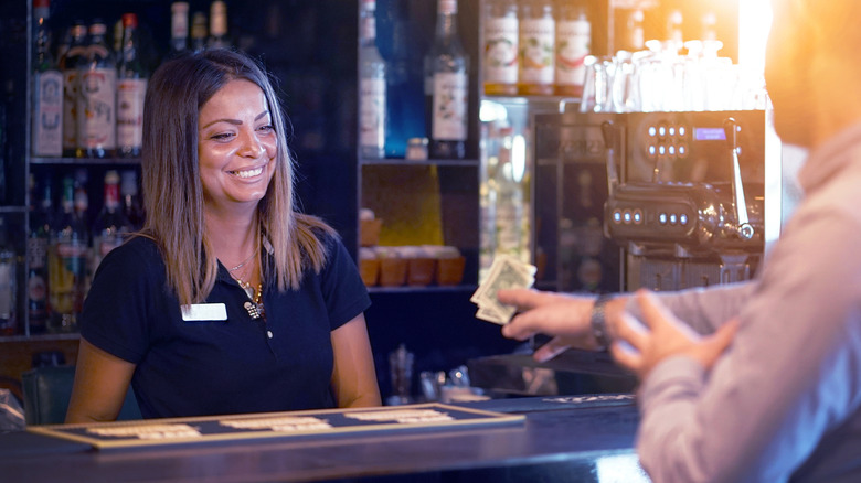 person hands tip over bar to pleased bartender