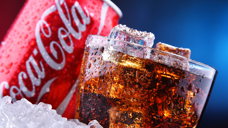 Close up of glass of cola with ice and coca cola in background