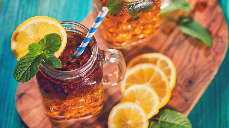 Aerial view of sweet tea with a striped straw in a mason jar glass, surrounded by lemons on a wooden board.