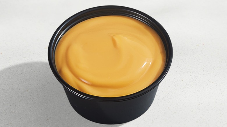 A black cup full of Taco Bell's nacho cheese sauce
