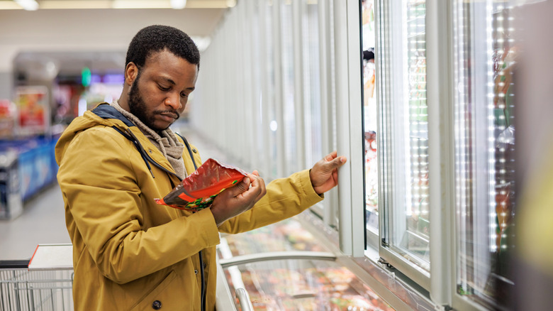 Man reading nutrition label on package of food in grocery store