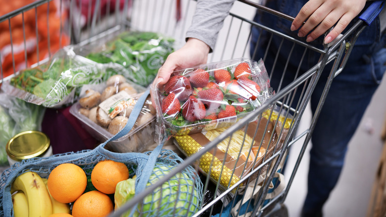 Hand putting strawberries in shopping cart full of fruits and vegetables