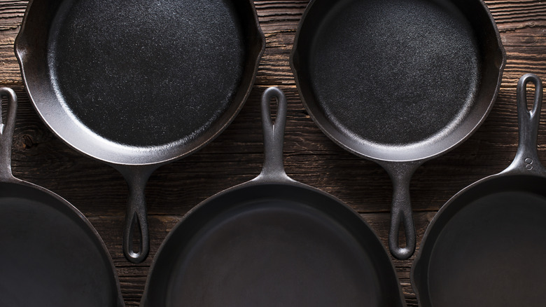 Several seasoned cast iron pans lined up in alternating directions on a wood table.