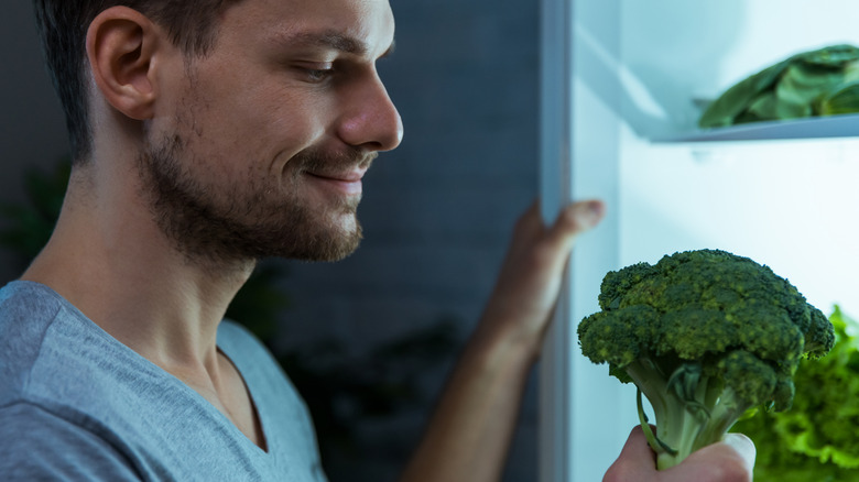 A man smiles while grabbing broccoli from the fridge.