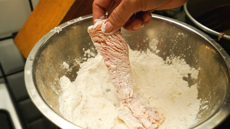 Hand dipping chicken into bowl of flour