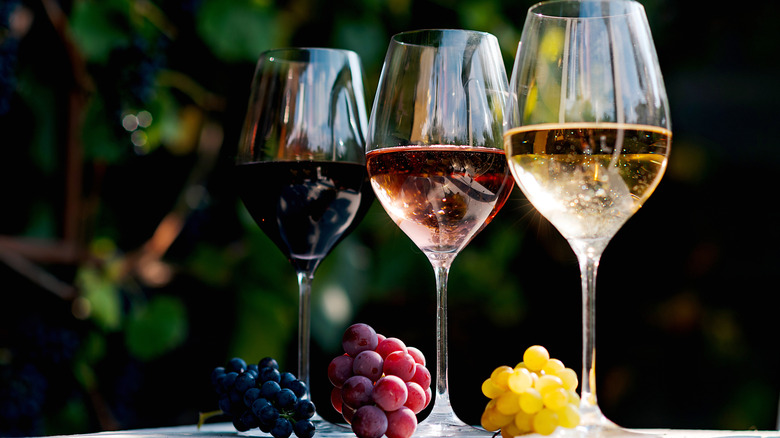 Three different glasses of wine made with purple, red, and green grapes.