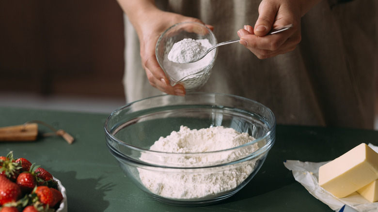 Spooning white powder into glass bowl of flour