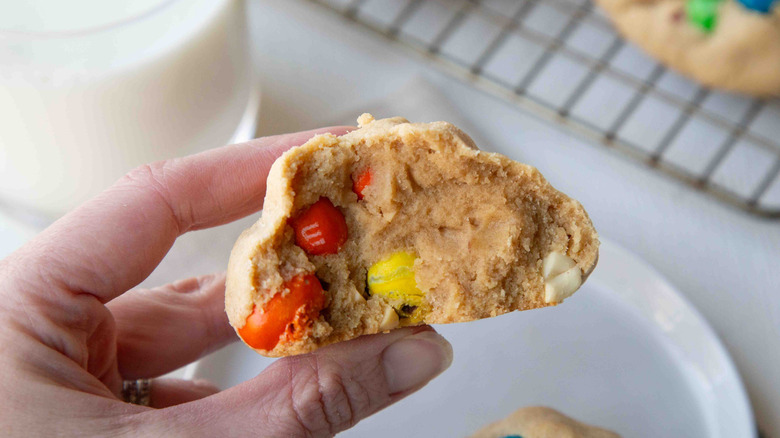 hand holding half of an M&M's cookie above a white plate